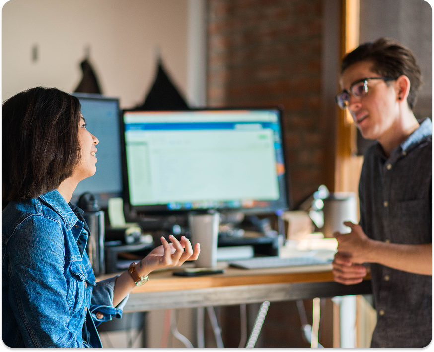 Built Mighty employees talking to each other at a desk with computers in the background