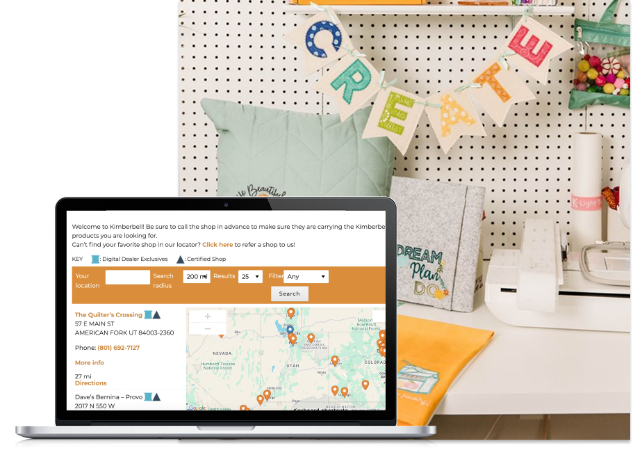 laptop showing kimberbell website store locator with an image behind it showing. acreative workstation desk
